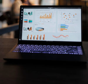 Computador portátil com análise de dados (gráficos de estatísticas) de marketing na tela, de pé sobre a mesa no escritório de inicialização, colegas de trabalho discutindo a estratégia da empresa em segundo plano.